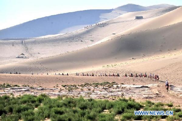 Tourists visit the scenic spot of Mingsha Mountain and Crescent Moon Lake by camel in Dunhuang City, northwest China's Gansu Province, July 29, 2011. This scenic spot received near 300,000 tourists in the past seven months, reaching a new high in recent years. [Xinhua/Gao Jianjun] 