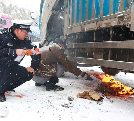 An officer helps a driver set a fire to warm his truck's frozen fuel tank on an expressway in Guizhou province on Wednesday, as the temperature dropped to - 6 C. [China Daily] 