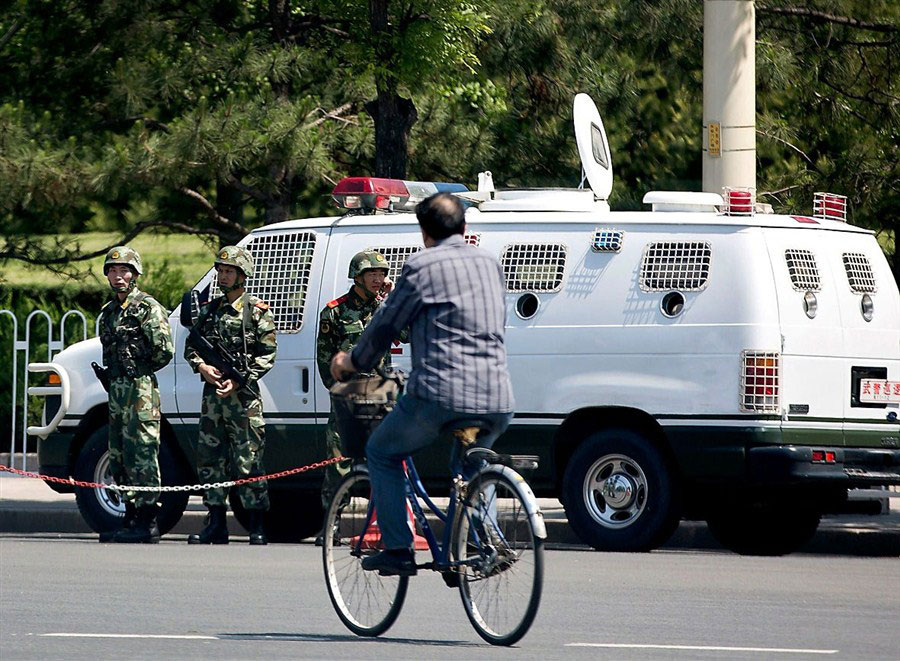 A cyclist passes by armed policemen standing guard near their vehicle on Chang'an Avenue in Beijing yesterday. The Chinese capital has deployed 150 such cars on the streets. [Photo/Shanghai Daily]